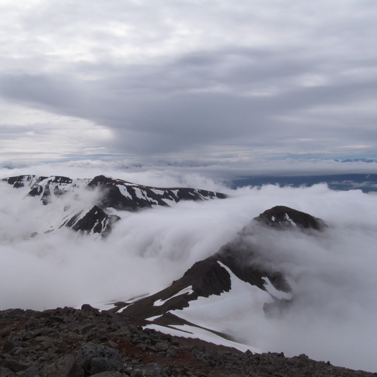 Þokan streymir niður Siglufjarðarskarð. Skarðshnjúkur og Illvirðishnjúkur standa upp úr.