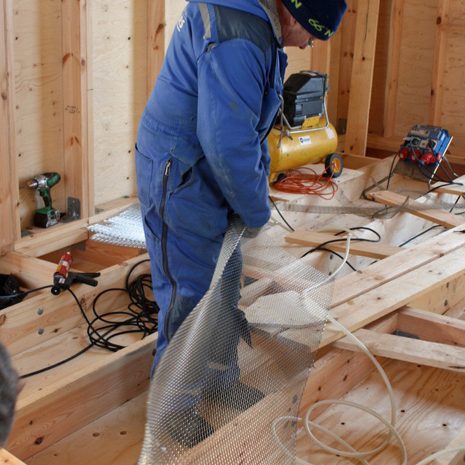 Hilmar að klippa til músanet í gólf skálans.